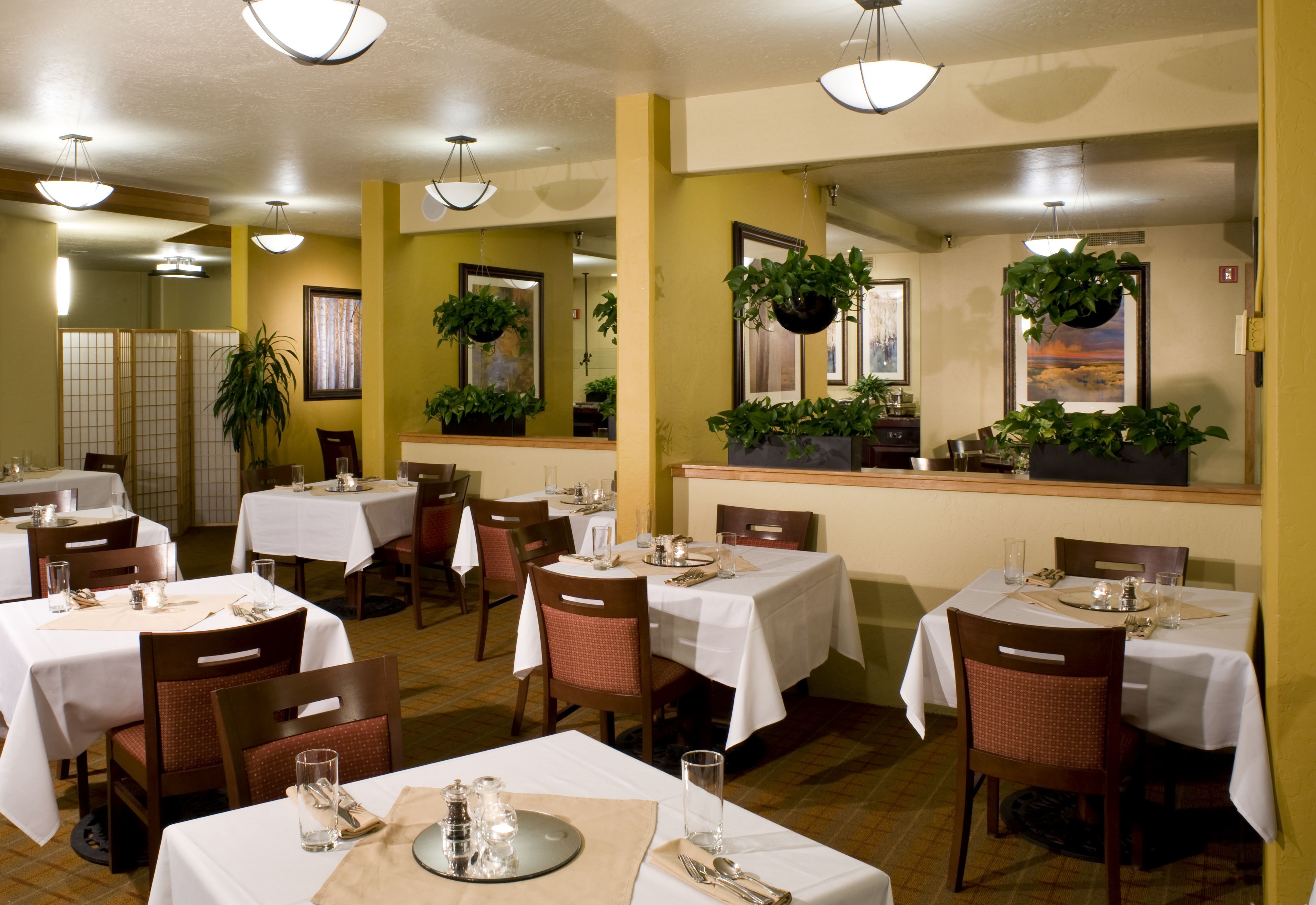 A restaurant with multiple tables set for dining, chairs, and hanging plants.