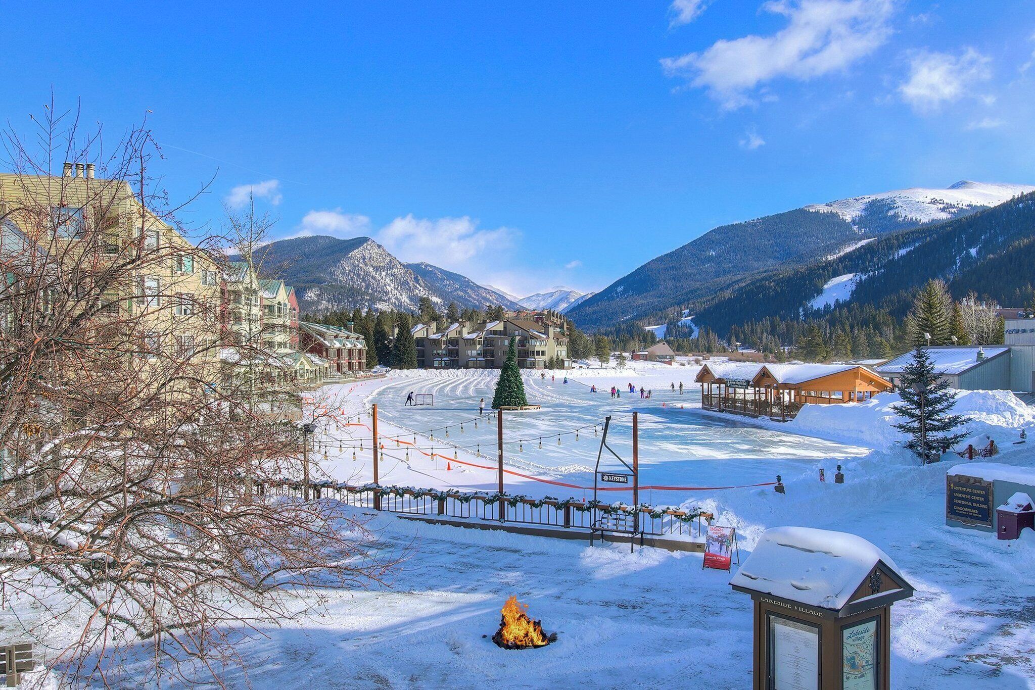 A snow-covered outdoor area with a wooden structure, a signboard, and a fenced area.