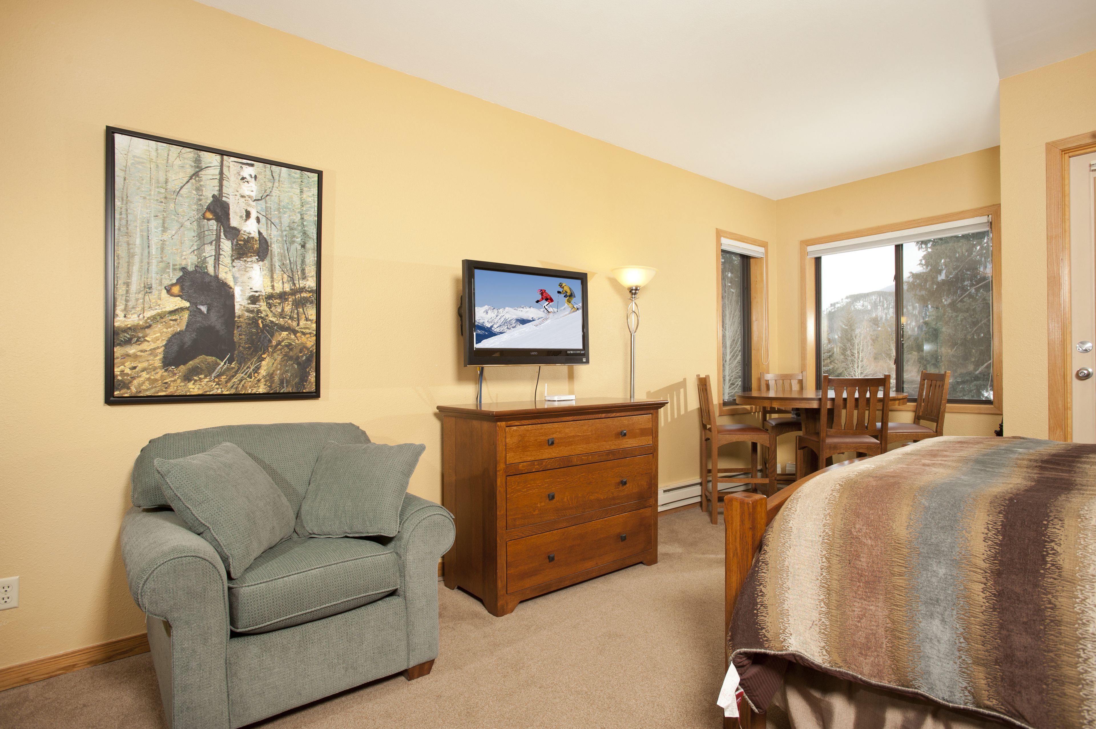 A bedroom with a bed, a dresser, a television, a couch, and a painting of bears.