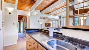 A modern kitchen with wooden beams, a large island with a sink, and a view of the outdoors. - Mountain House, A Vail Resorts Property (Keystone)