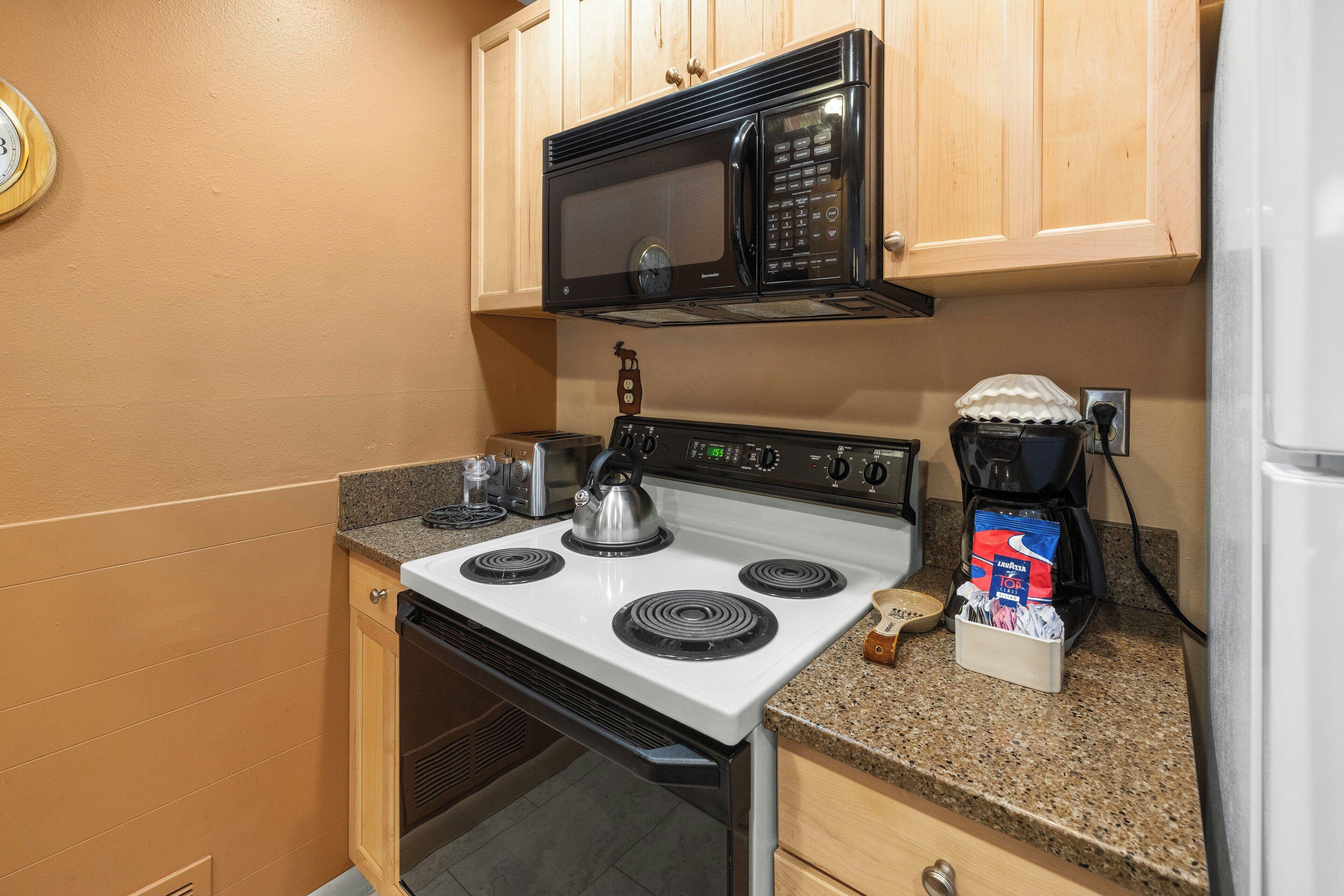 A kitchen with a white stove, a black microwave, wooden cabinets, and a coffee maker on the counter.