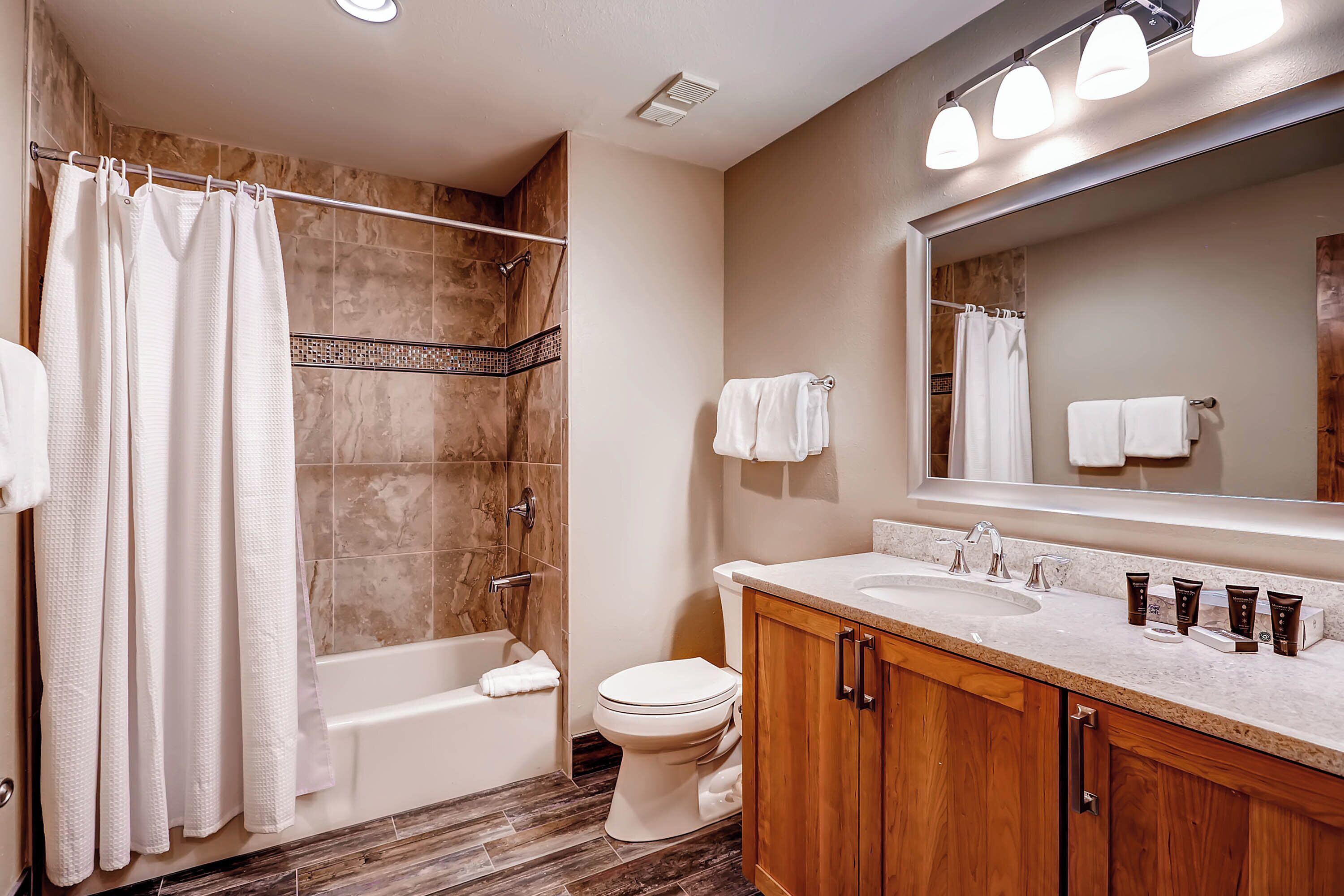 A modern bathroom with a bathtub, toilet, and vanity with a sink and mirror.