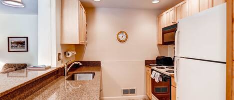 A compact kitchen with granite countertops, wooden cabinets, a built-in oven, and a refrigerator.
