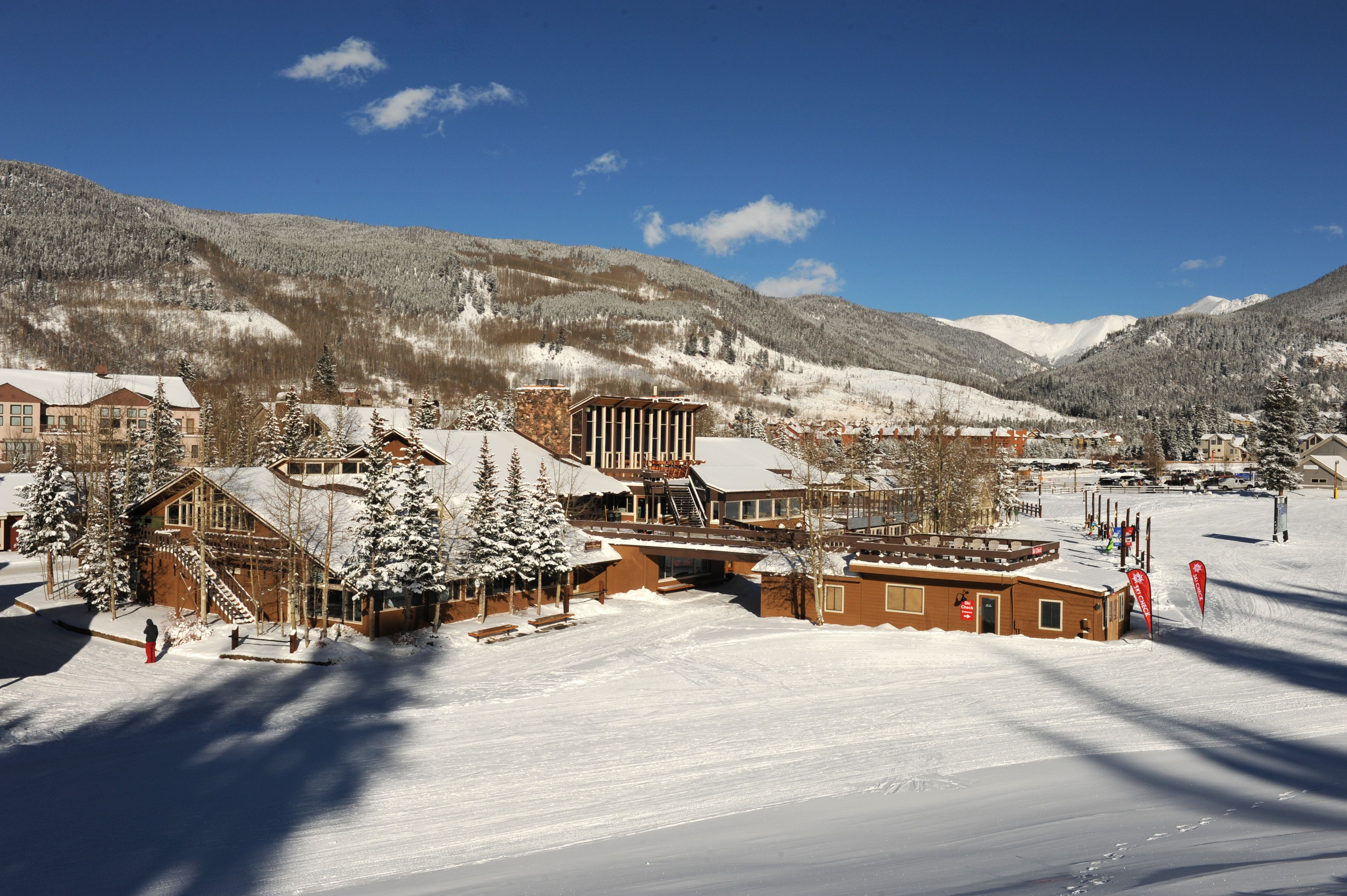 Ein schneebedecktes Bergresort mit mehreren Gebäuden, darunter eine Berghütte und eine Seilbahn, vor einer Kulisse aus verschneiten Bäumen und Bergen.