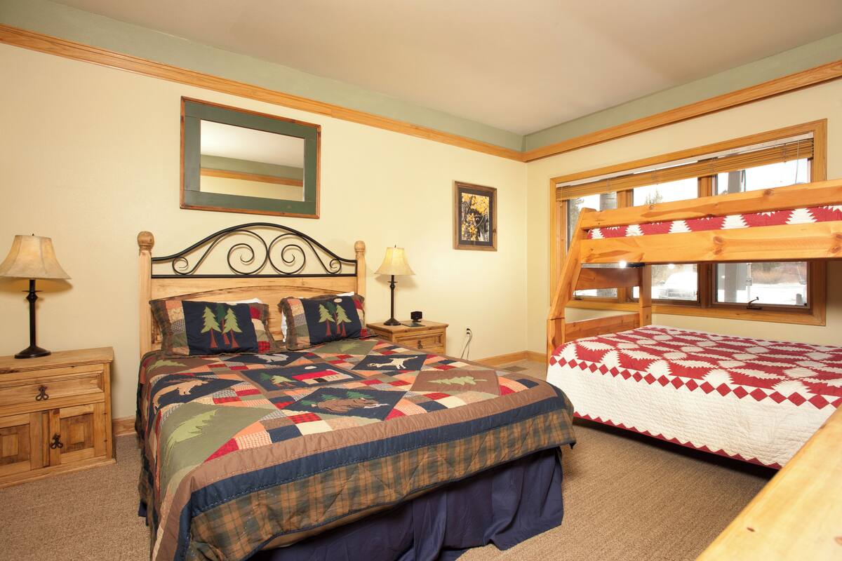 A bedroom with a large bed, a smaller bed, wooden headboard, nightstands, lamps, a mirror, and a window with a view.