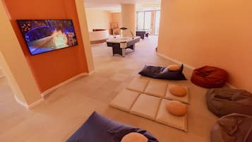 Una sala de estar moderna con un televisor de pantalla plana, una mesa de billar y una zona de estar con cojines.