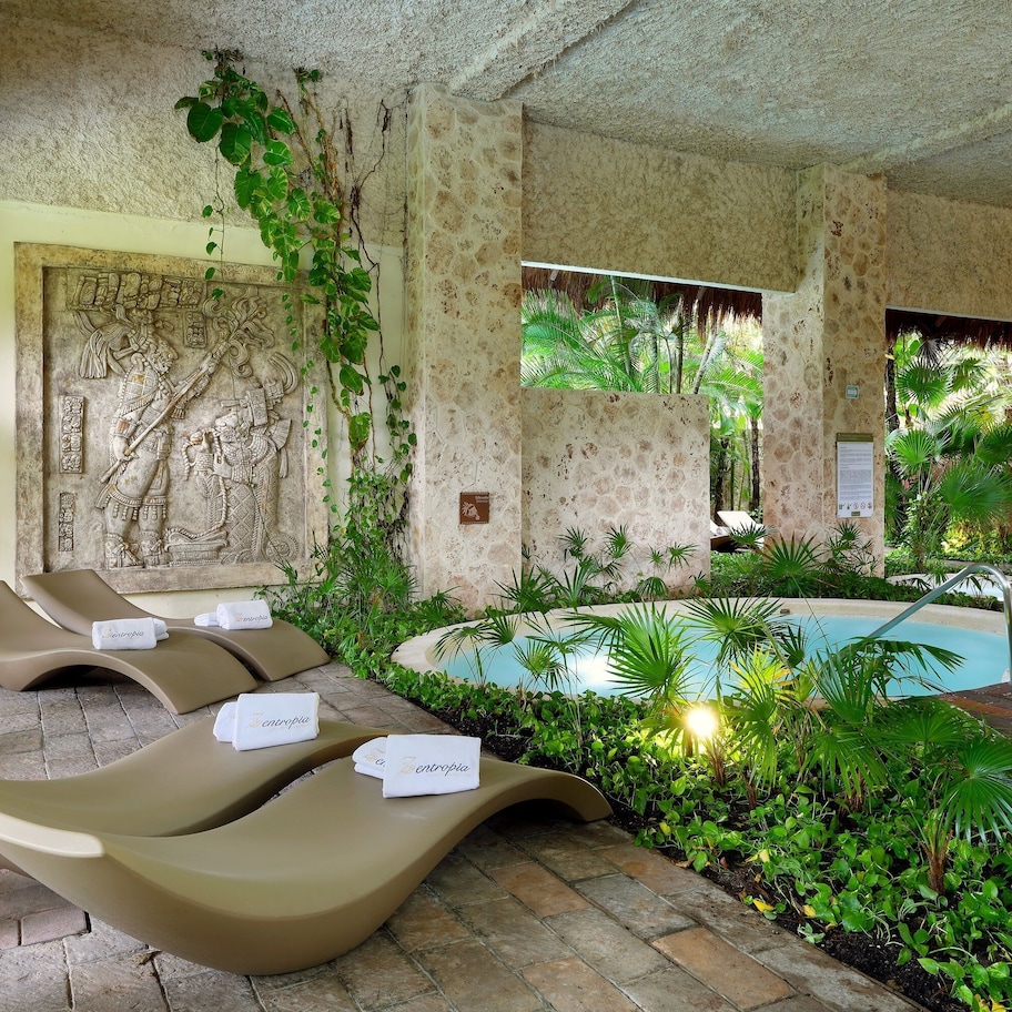 A poolside area with lounge chairs and a pool, surrounded by lush greenery and stone walls.