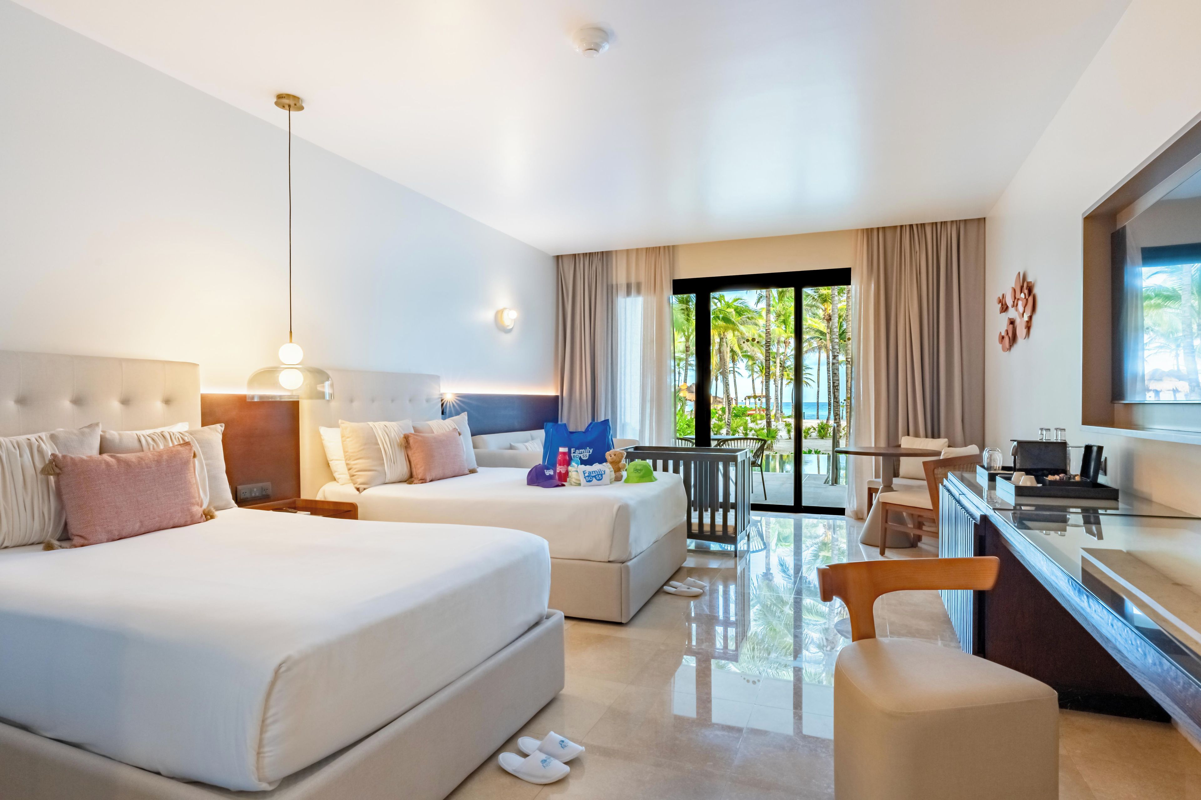 Een hotelkamer met twee bedden, een bureau, een stoel, een zithoek en uitzicht op palmbomen.