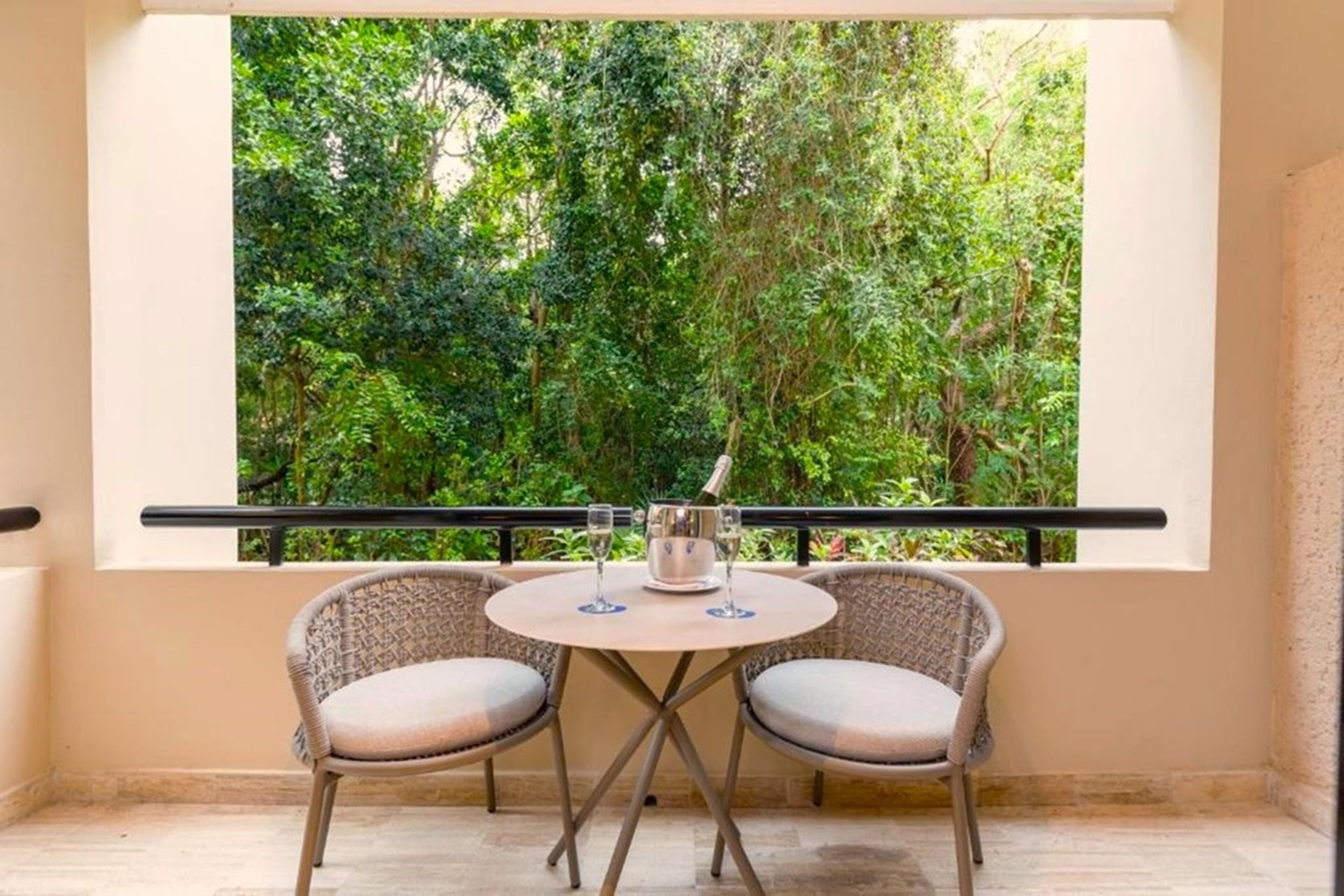 A balcony with two wicker chairs and a small round table, overlooking a lush green garden.