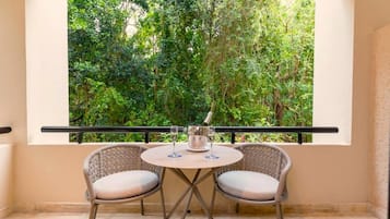 A balcony with two wicker chairs and a small round table, overlooking a lush green garden.
