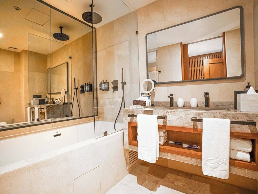 A modern bathroom with a large mirror, a bathtub, and a vanity with a wooden shelf.
