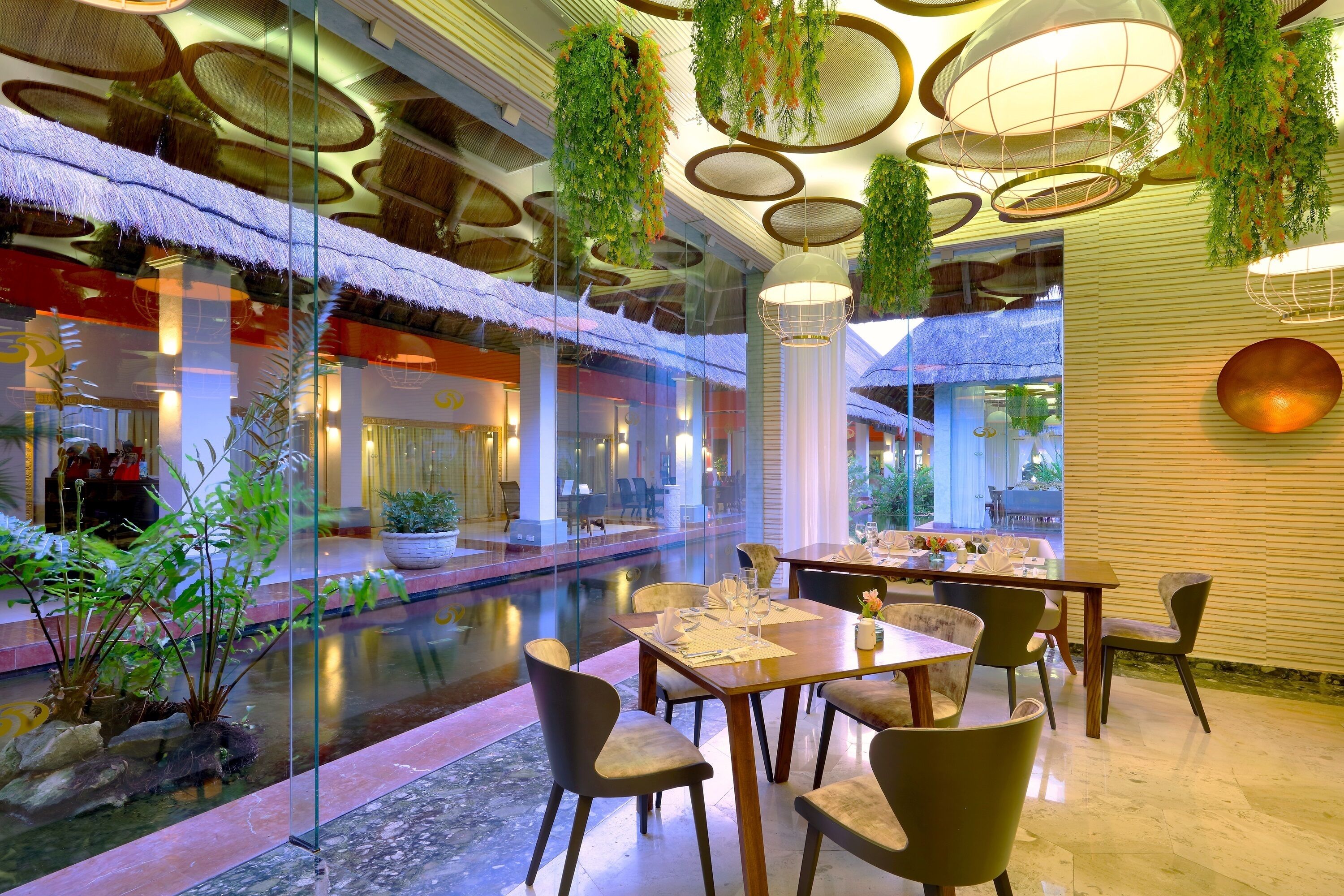 Un comedor interior moderno con paredes de vidrio, una fuente de agua y plantas colgantes.