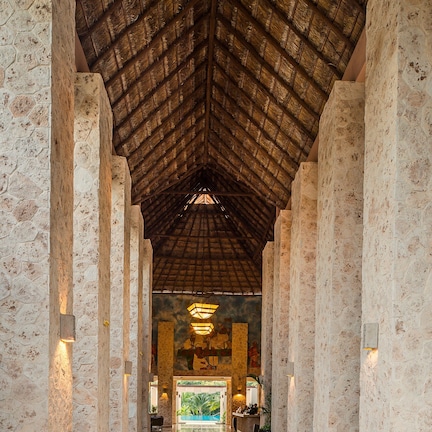 A corridor with stone columns, a wooden ceiling, and a view of an outdoor pool area.