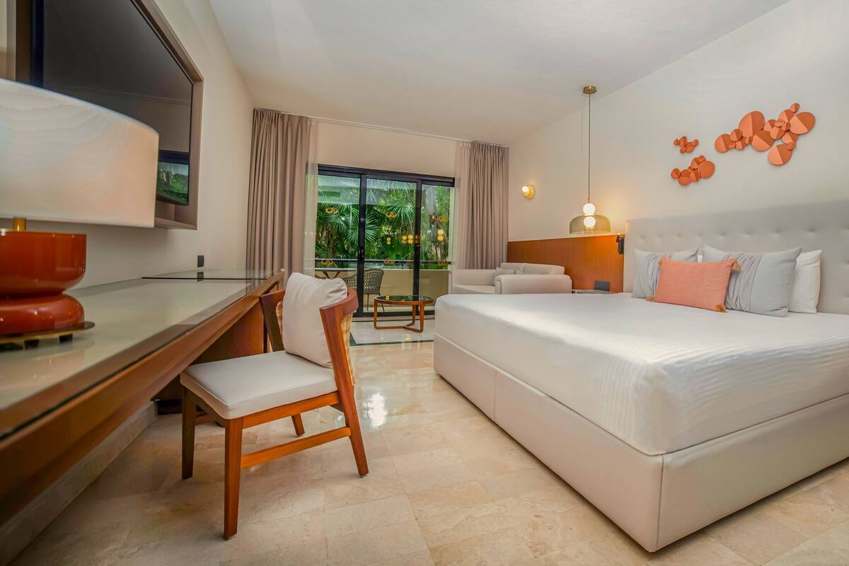 A hotel room with a bed, a desk, a chair, a TV, and a balcony with curtains.