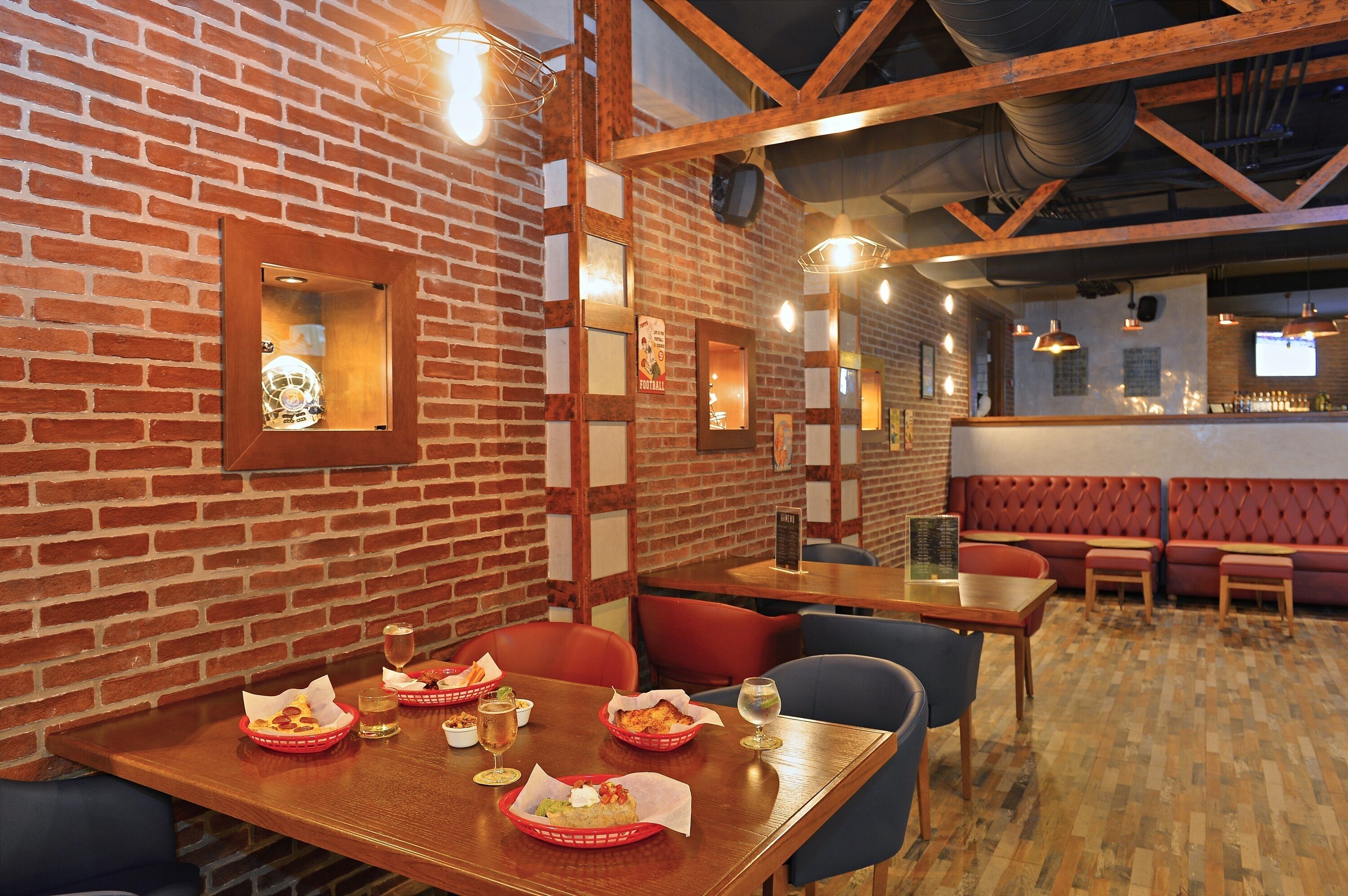 Un restaurante con paredes de ladrillo, vigas de madera y una zona de bar. Las mesas están dispuestas con cestas de comida y bebidas.