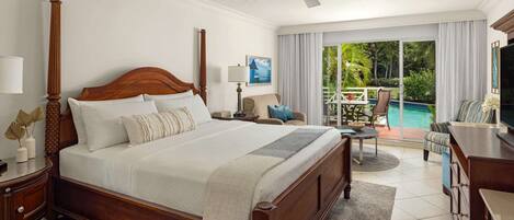 A spacious bedroom with a large bed, a ceiling fan, a nightstand, a lamp, and a view of a pool and outdoor seating area.