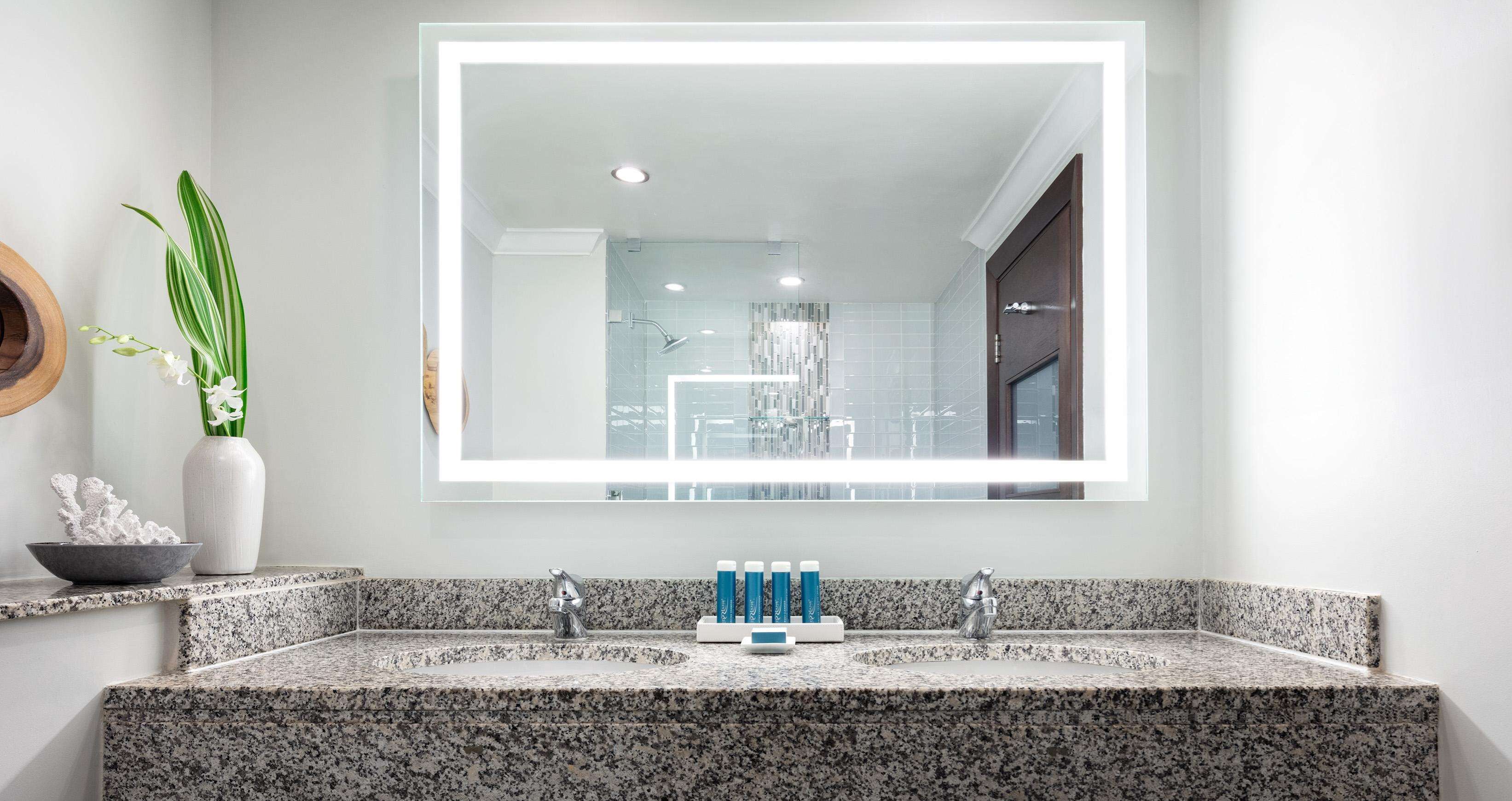 A bathroom with a granite countertop, a large mirror, and a shower area visible through the glass door.