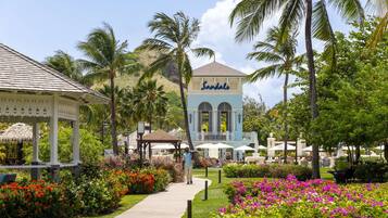 A resort with a gazebo, a building labeled "Sandals", and a pathway surrounded by colorful flowers and palm trees.