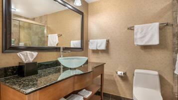 A modern bathroom with a glass sink, wooden vanity, a large mirror, and a toilet.