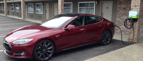 Une Tesla Model S rouge est garée sur un parking, avec un bâtiment en briques en arrière-plan.