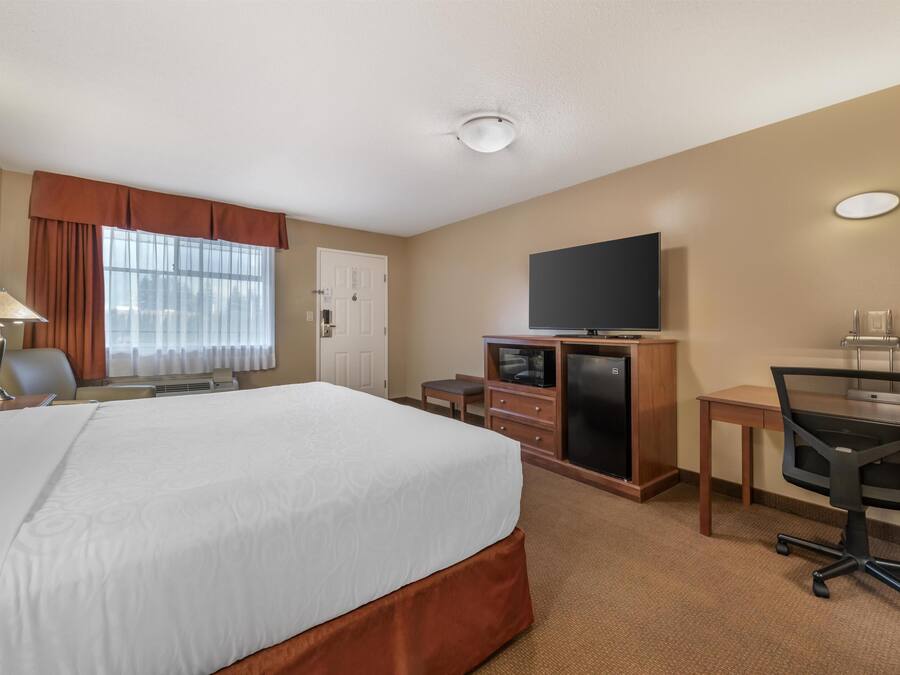 A hotel room with a large bed, a desk with a computer, a television, and a window with curtains.