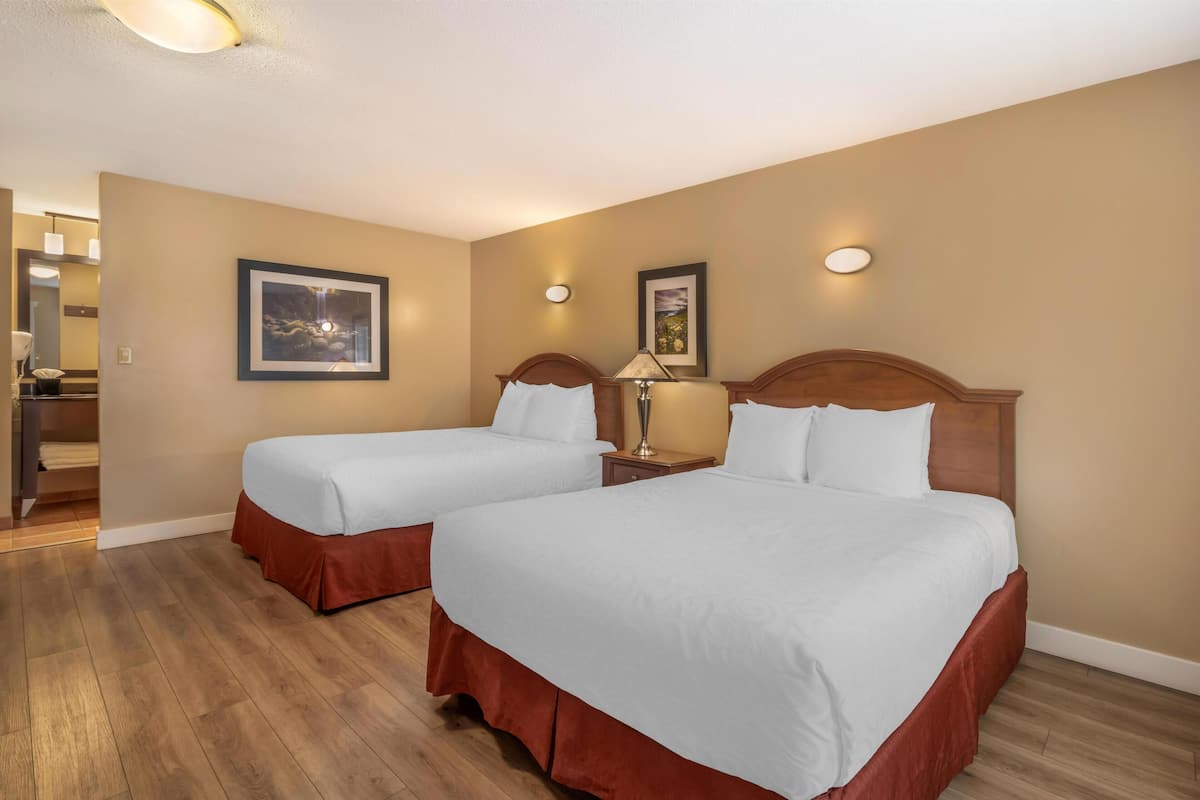 A hotel room with two beds, wooden flooring, and beige walls.