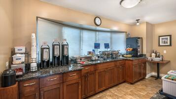 A kitchen with wooden cabinets, a granite countertop, a coffee station, and a clock on the wall.