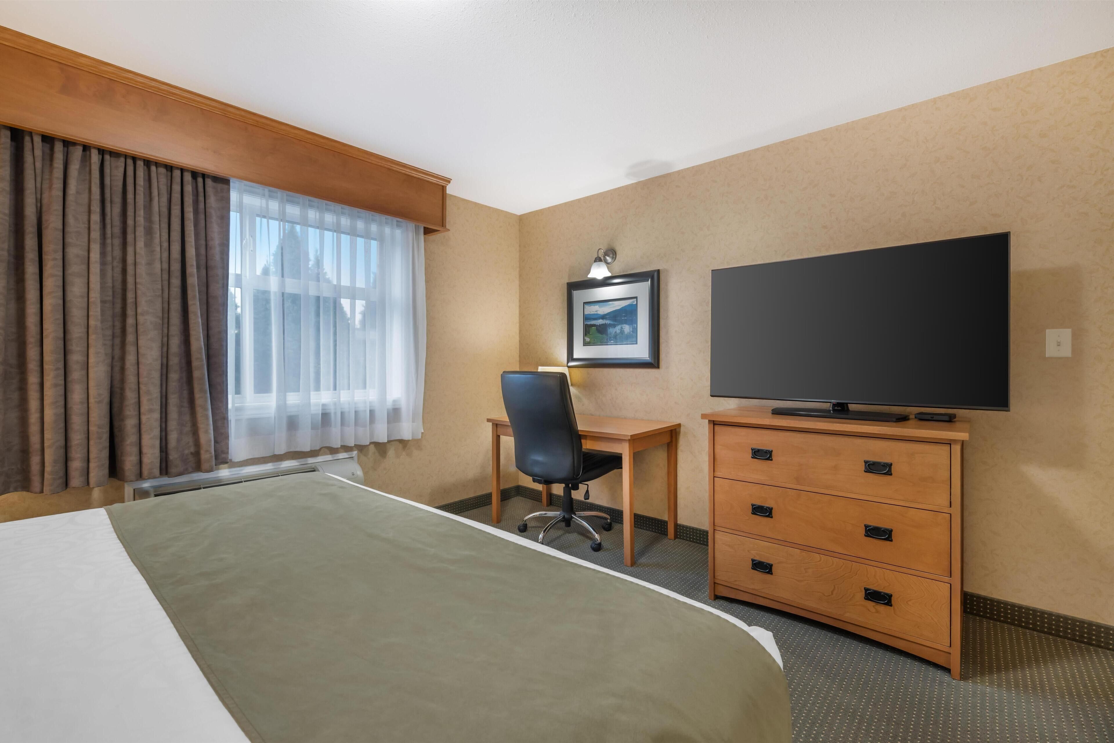 A hotel room with a bed, a desk, a chair, a television, and a dresser.