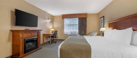 A hotel room with a bed, a television, a desk with a chair, a fireplace, and a window with curtains.