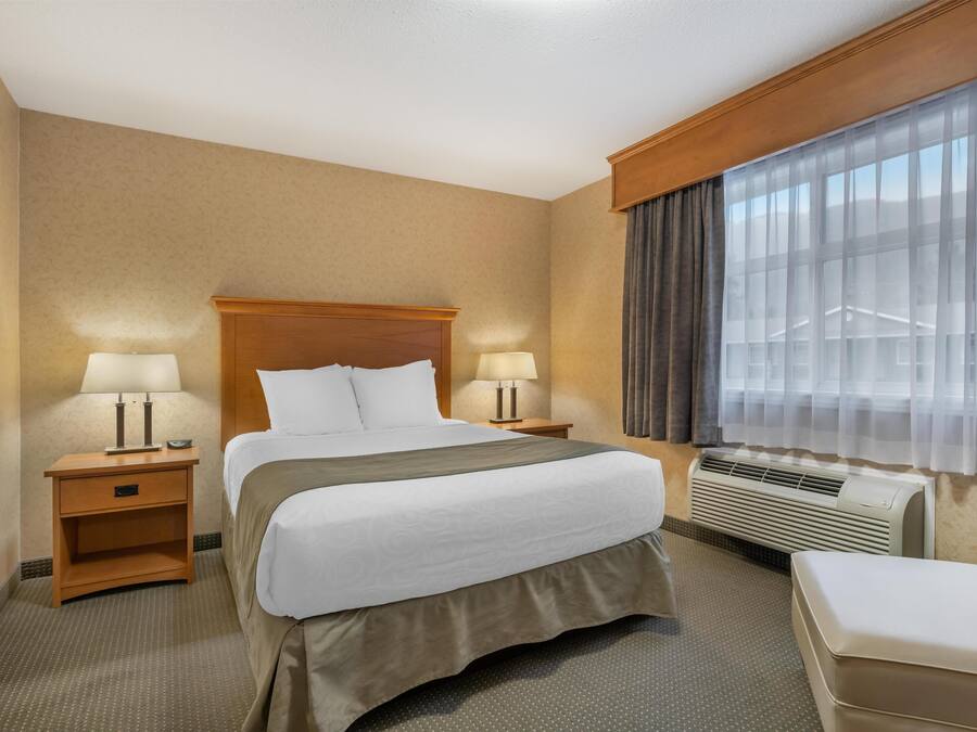 Ett hotellrum med en stor säng, två sängbord med lampor, ett fönster med gardiner och en luftkonditioneringsanläggning.