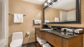 Un baño moderno con un inodoro blanco, un lavamanos con espejo y toallas ordenadas en un perchero.
