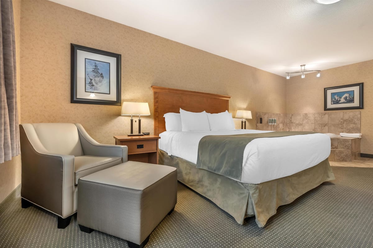 A hotel room with a large bed, a chair, a small table, and two wall-mounted lamps.