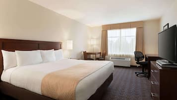 A hotel room with a large bed, a desk, a chair, a television, and a window with curtains.