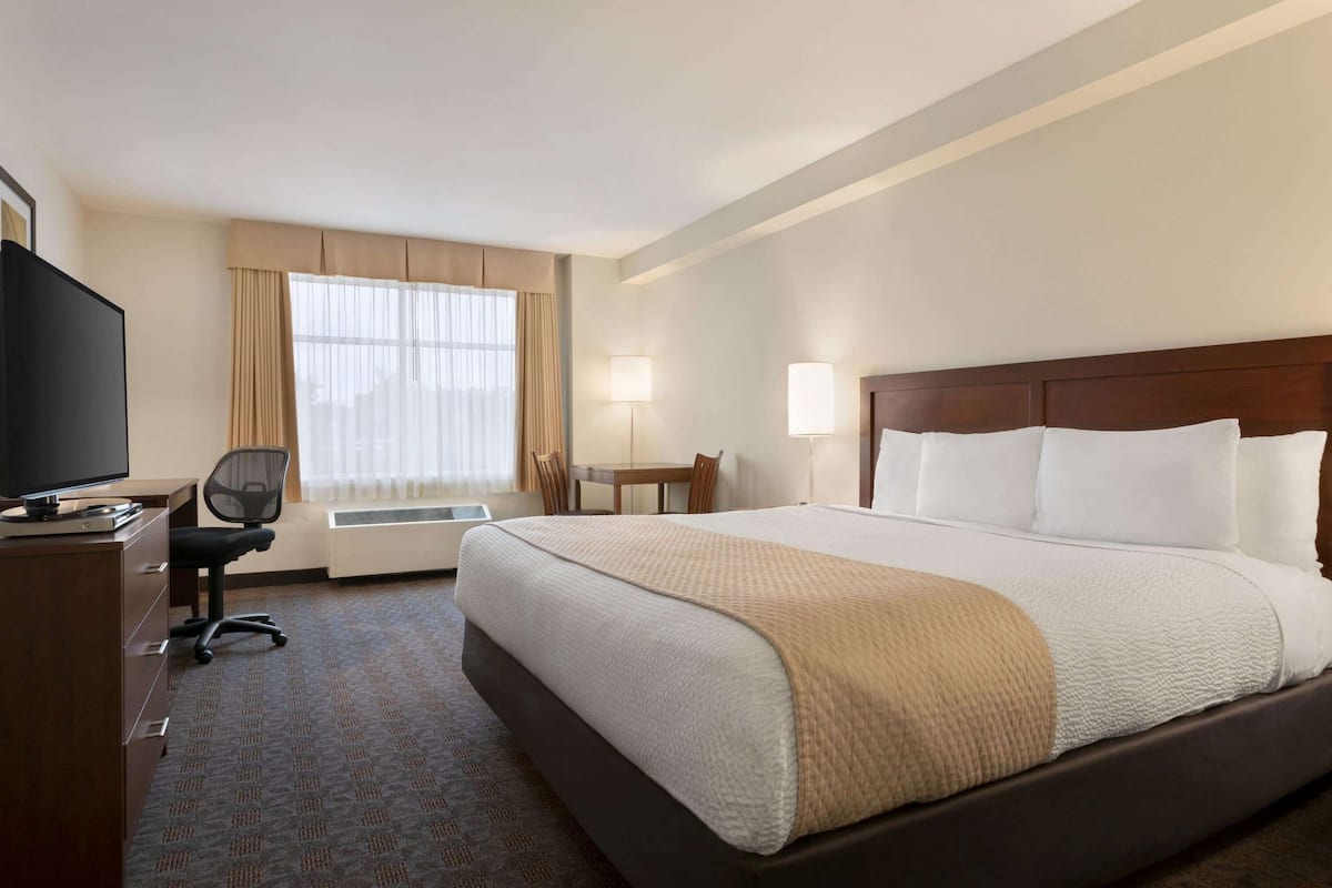 Une chambre d’hôtel avec un grand lit, un bureau avec une télévision, une chaise, une fenêtre avec des rideaux et une table de chevet.