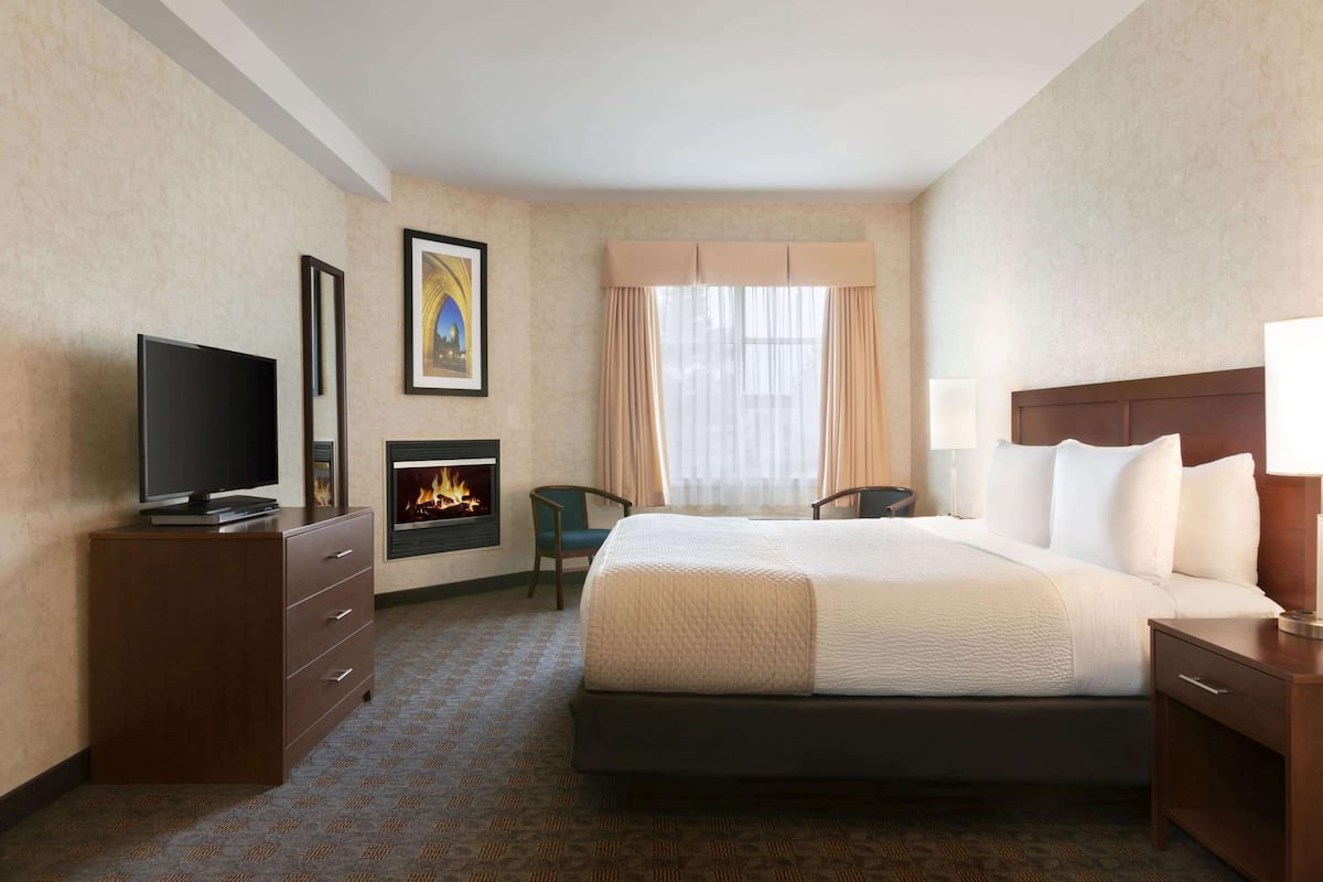 Une chambre d’hôtel équipée d’un lit, d’une télévision, d’une cheminée, d’un bureau et d’une fenêtre avec des rideaux.