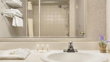 A bathroom with a sink, mirror, towels, toiletries, and a shower.