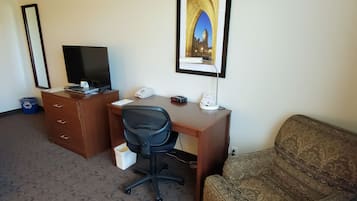 Een hotelkamer met een houten bureau, een zwarte bureaustoel, een televisie, een afgebeldde afbeelding van een brug en een gestreept sofa.