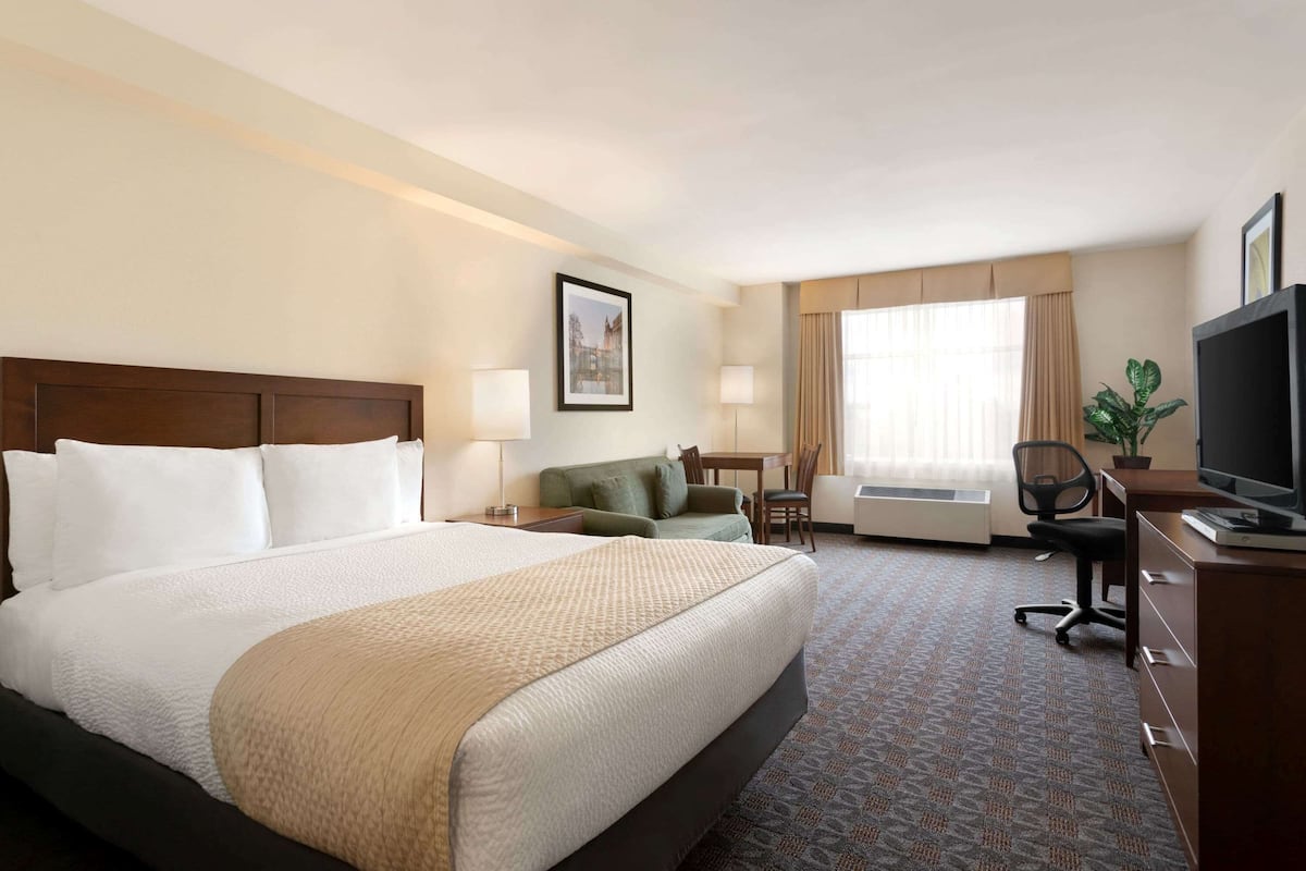 Une chambre d’hôtel avec un grand lit, un bureau avec un ordinateur, une chaise, une télévision et une fenêtre avec des rideaux.