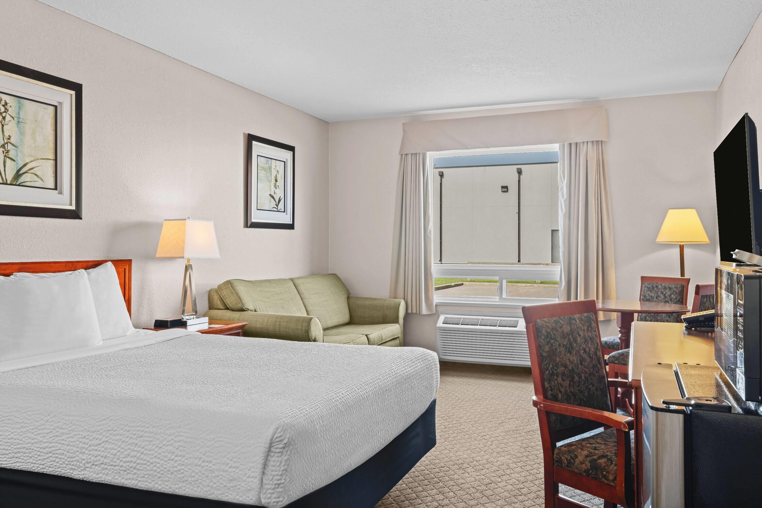 A hotel room with a large bed, a green sofa, a desk with a chair, and a television.
