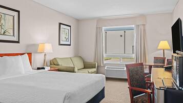 A hotel room with a large bed, a green sofa, a desk with a chair, and a television.