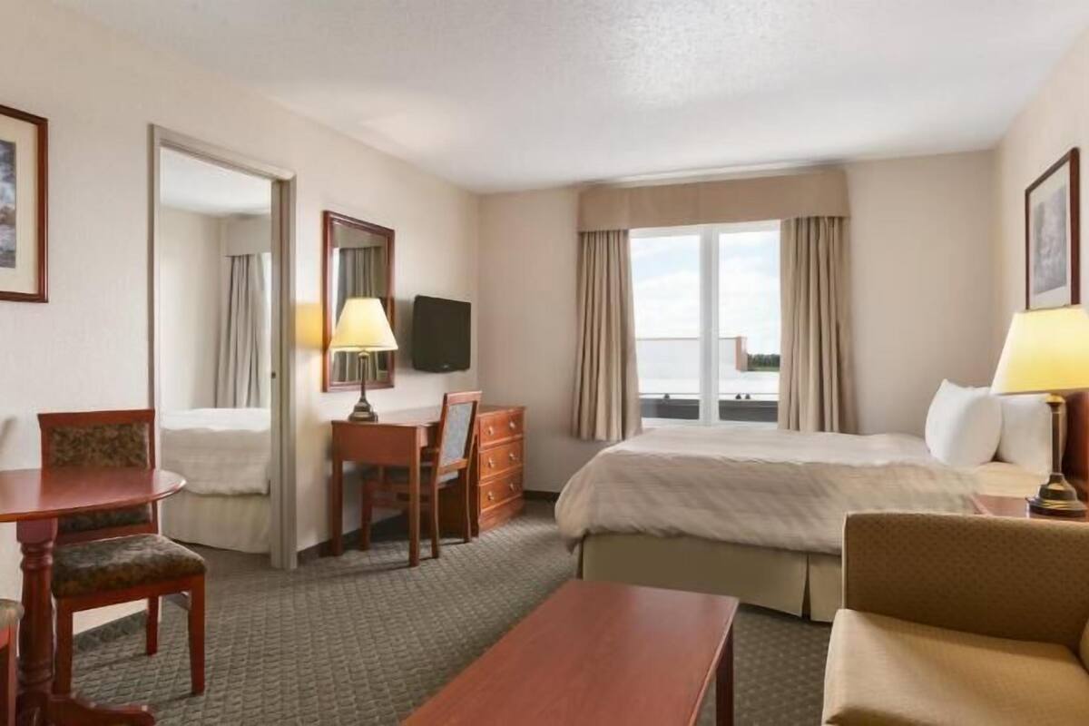 A hotel room with a bed, desk, chair, and a TV.