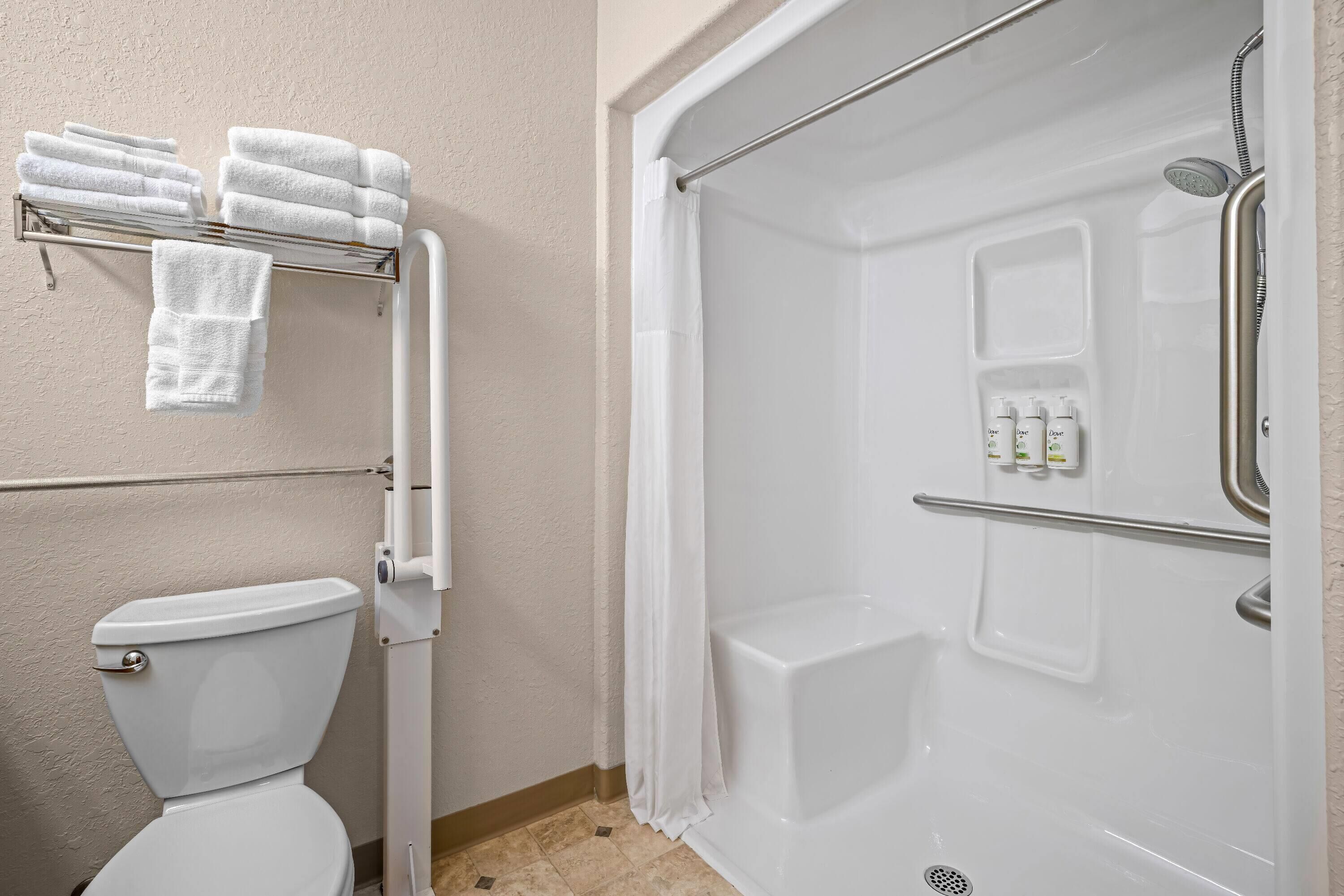 Un bagno con il water, una doccia dotata di maniglione e un portasciugamani con asciugamani piegati.