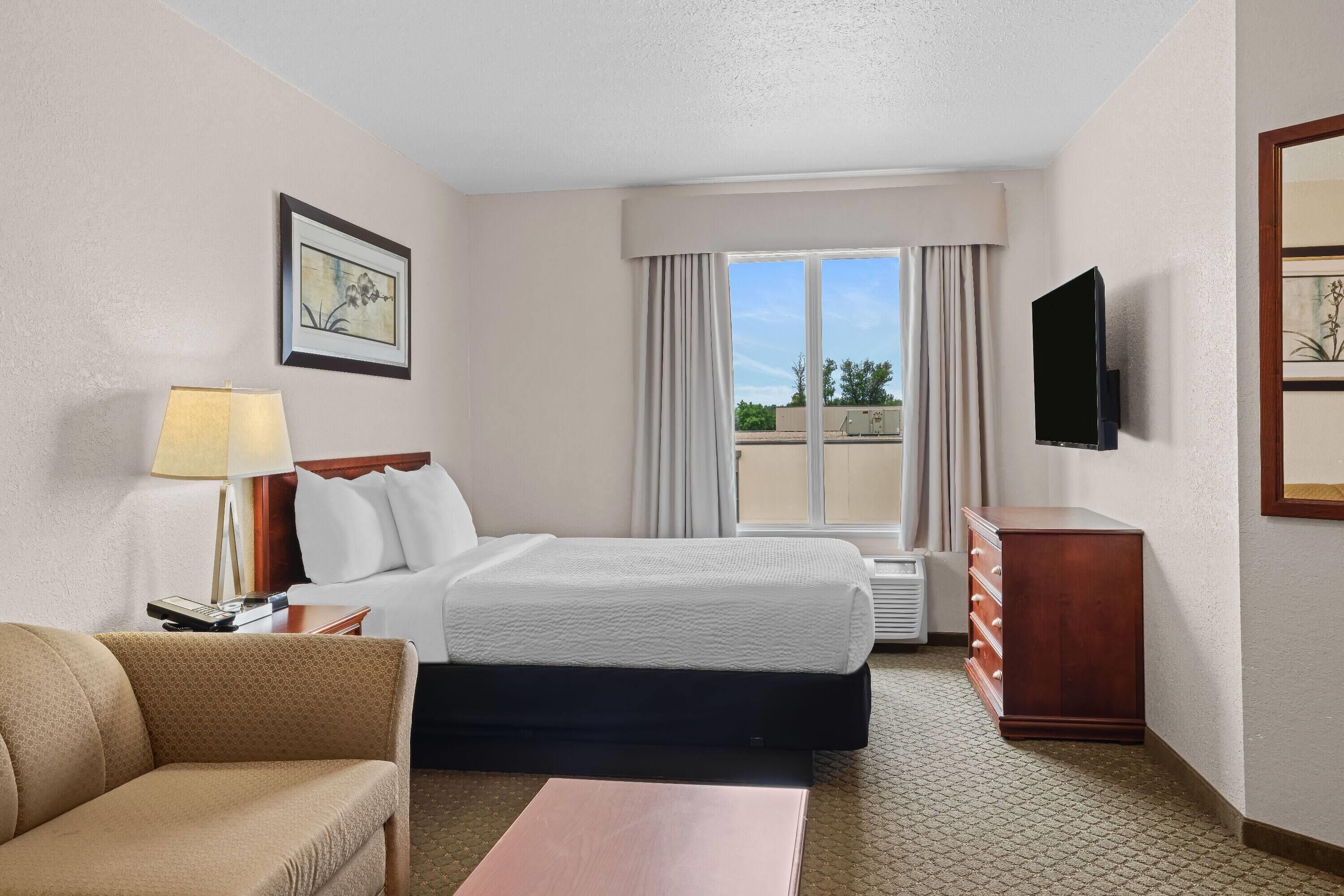 A hotel room with a bed, a TV, a desk, a lamp, and a window with curtains.