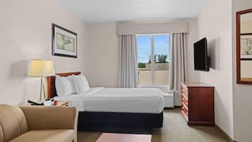 A hotel room with a bed, a TV, a desk, a lamp, and a window with curtains.