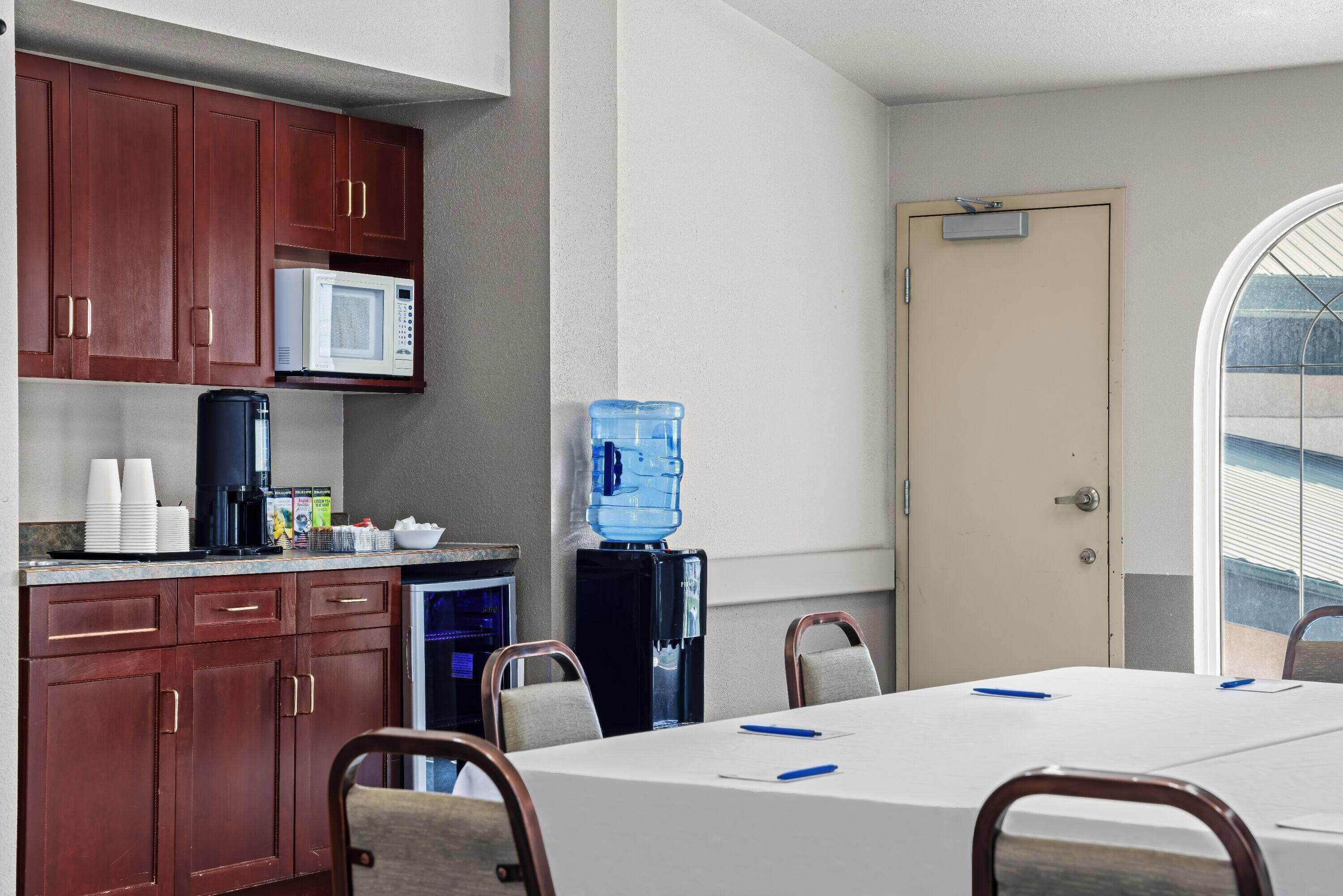A conference room with a white table, brown chairs, a water cooler, a microwave, and a coffee machine.