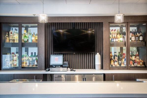 Una zona de bar moderna con una televisión de pantalla plana, una caja registradora y estantes llenos de botellas de licores.