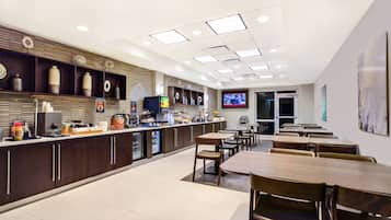 A modern restaurant with a long counter, wooden chairs, and a television screen.
