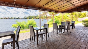 An outdoor patio with a covered seating area overlooking a body of water, surrounded by greenery.