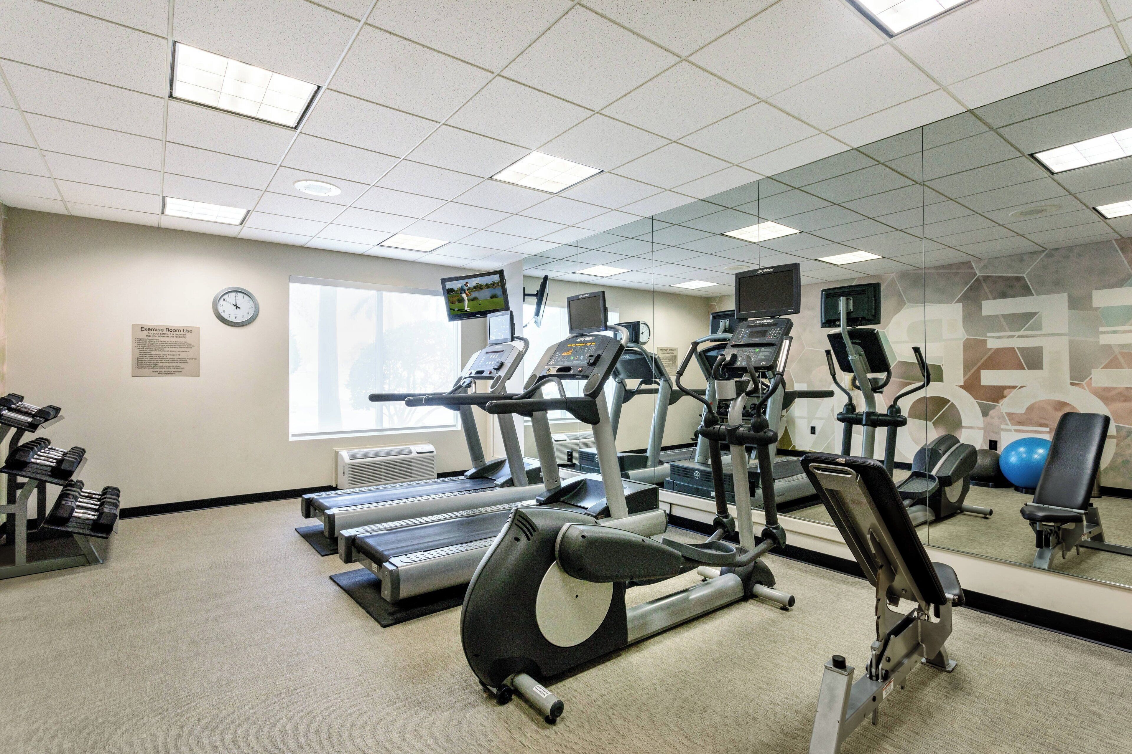 Une salle de sport équipée de tapis de course, de vélos elliptiques et de poids libres.