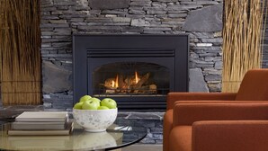 Una sala de estar moderna con chimenea de piedra, una mesa de centro de vidrio y un sofá naranja.